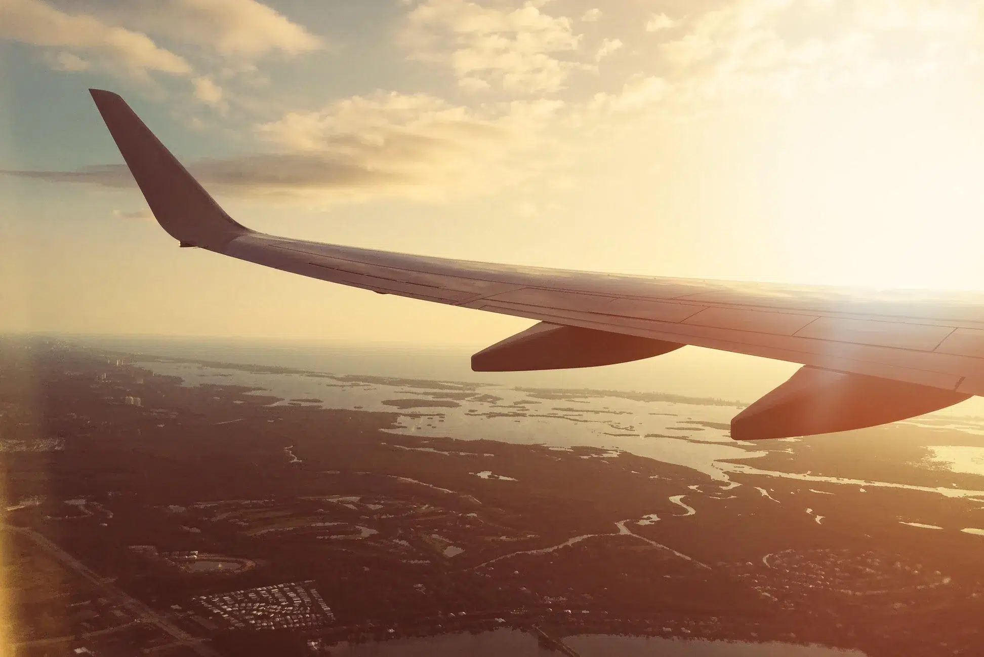 An image from an aeroplane window of an aeroplane wing against the sunset on land
