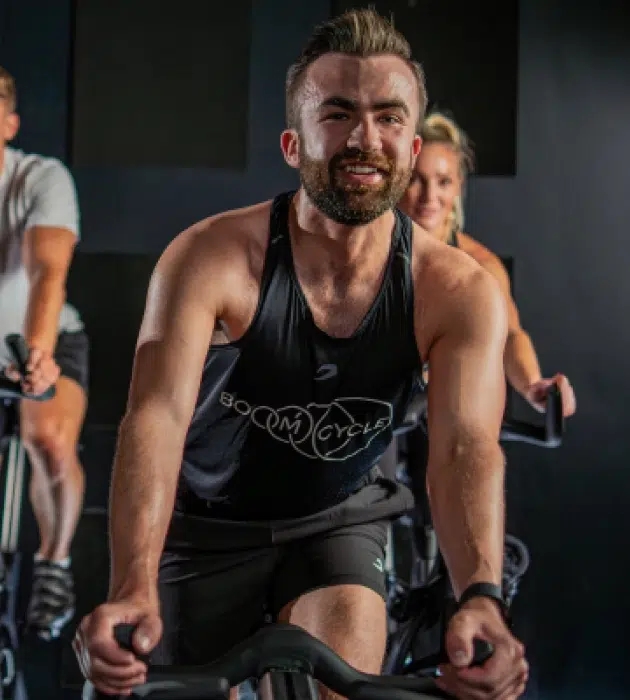 Boom Cycle riders mid-class, led by an energetic instructor in a high-intensity indoor cycling session set to music and mood lighting.