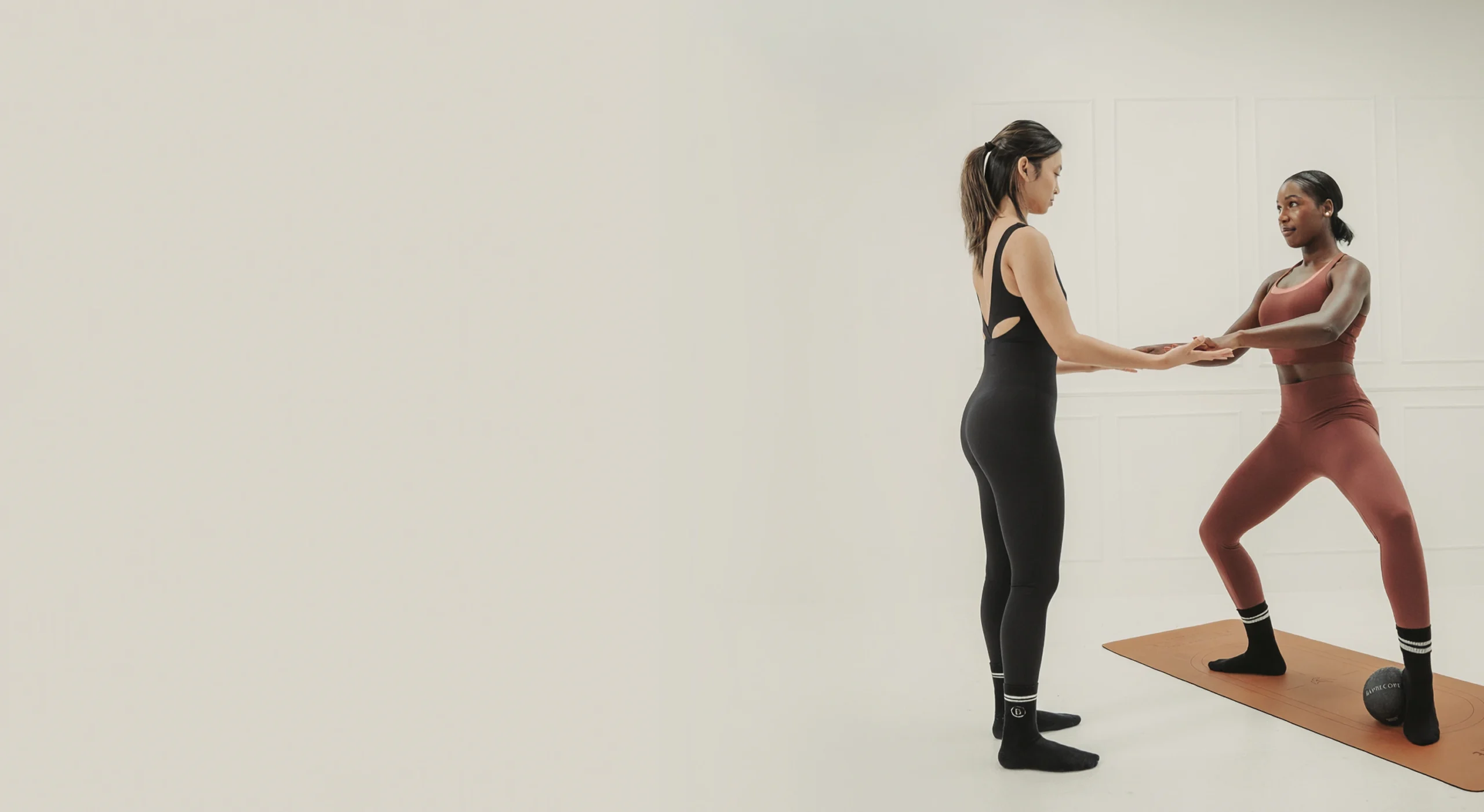 Barrecore instructor guiding a client through a plié position on a mat, with a Barrecore ball placed under her heels